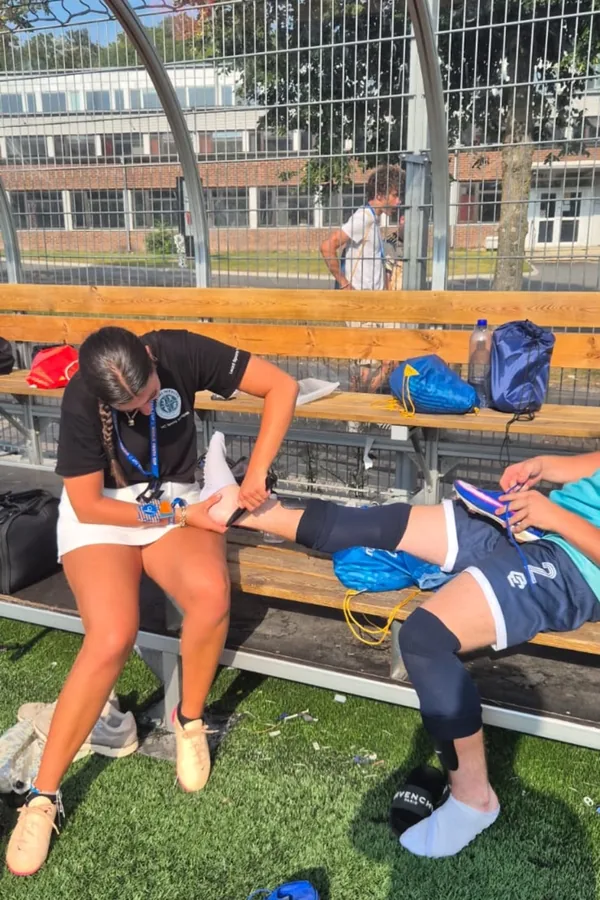 Mia strapping a young player's ankle on the substitutes' bench at the Gothia Cup