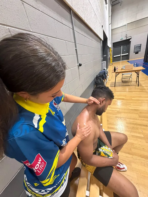 Mia working on a Kabaddi player's shoulder courtside in a sports hall