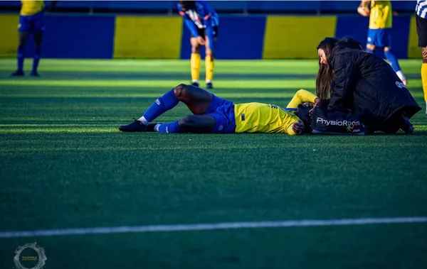 Mia kneeling over an injured player on the floodlit pitch during a match