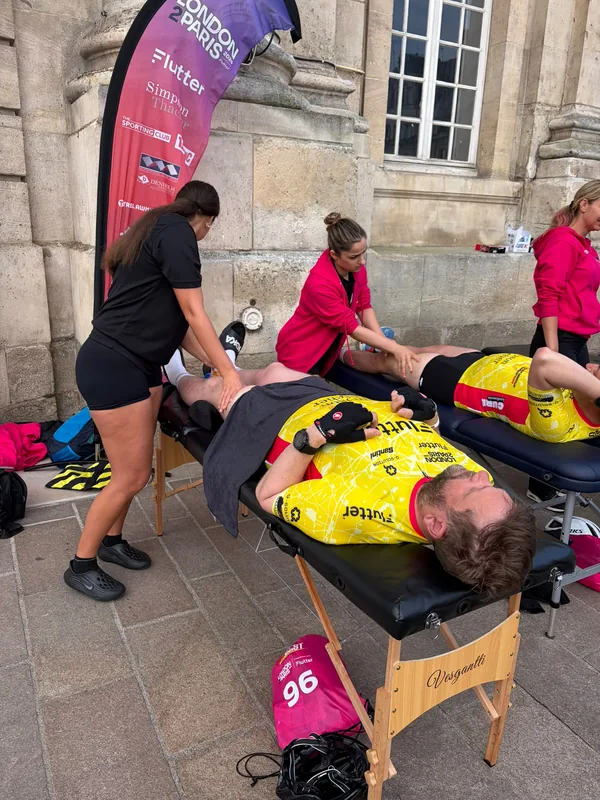 Two therapists working on cyclists on treatment couches outside a French church