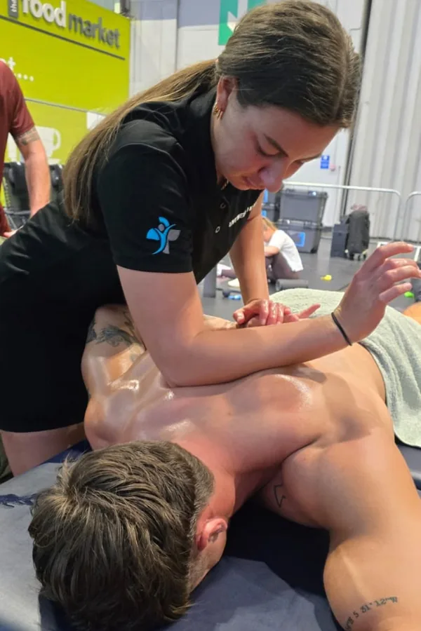 Mia delivering a back massage on a treatment couch inside an exhibition hall