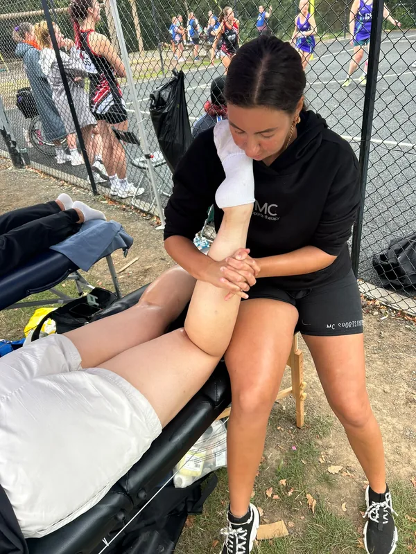 Mia in branded MC Sports Therapy kit treating a netball player's calf courtside