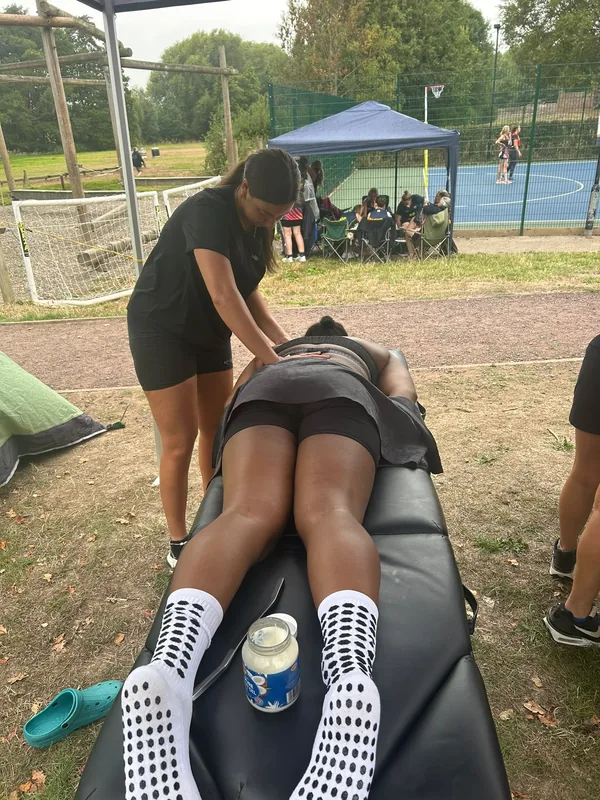 A treatment couch set up on grass beside netball courts with a player receiving back work
