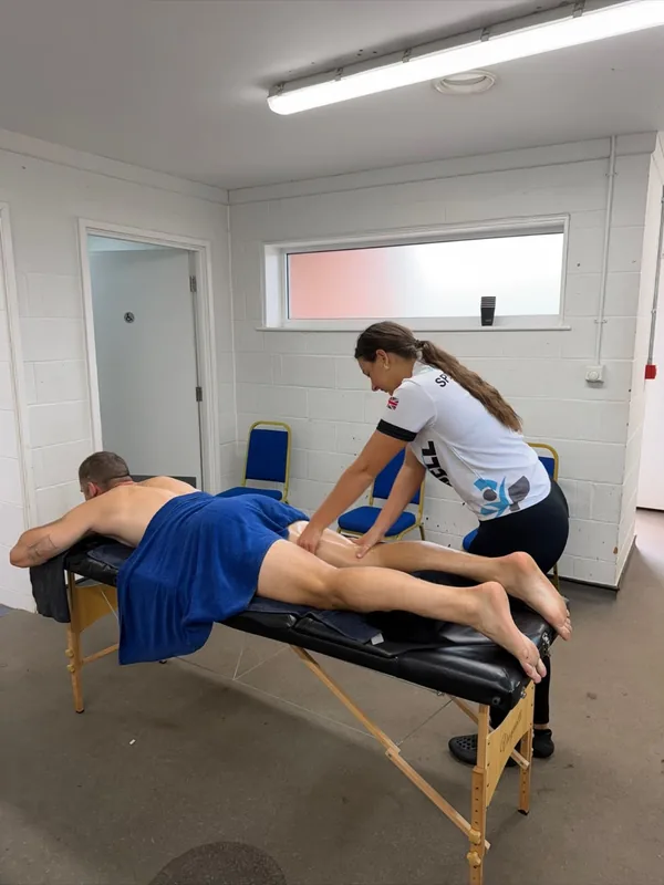 Mia working along a client's hamstring on a portable couch in a clinic room