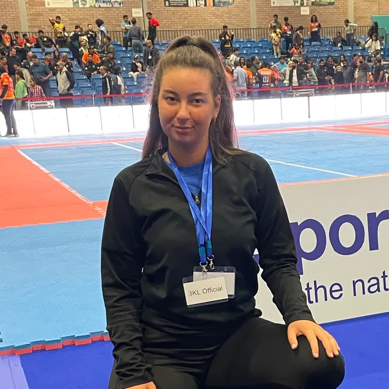 Mia Cole in black therapist kit kneeling beside her kit bags at a Kabaddi tournament in Glasgow
