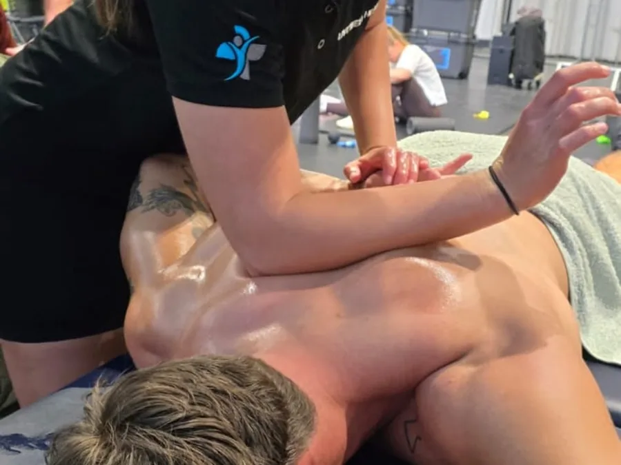 Mia delivering a recovery massage on a treatment couch in a busy exhibition hall