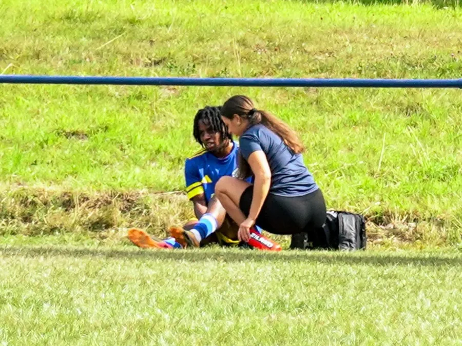 Mia assessing a footballer's lower leg pitch-side, kit bag open beside her