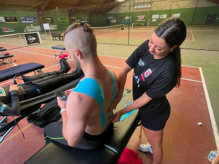 Blue kinesiology tape being applied across a cyclist's upper back and shoulder